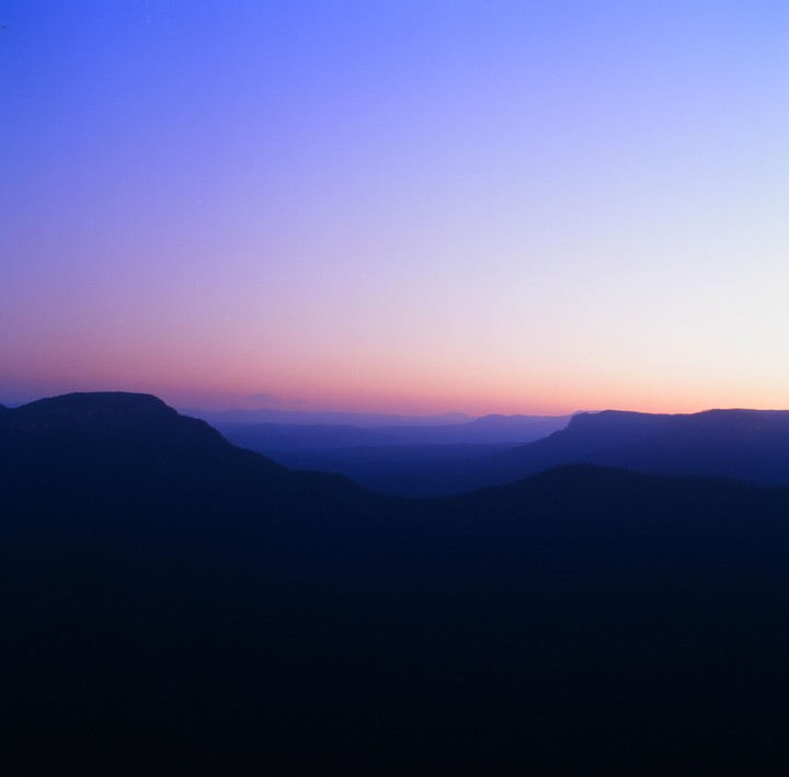 A mountain range is silhouetted against a colorful sky at dusk.