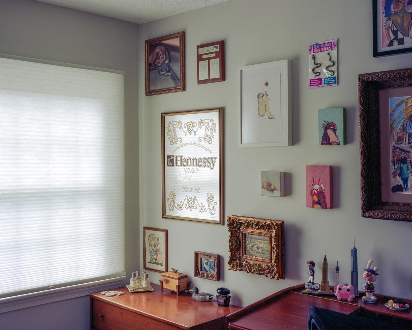 A collection of framed art and objects are displayed on a gray wall and wooden furniture.