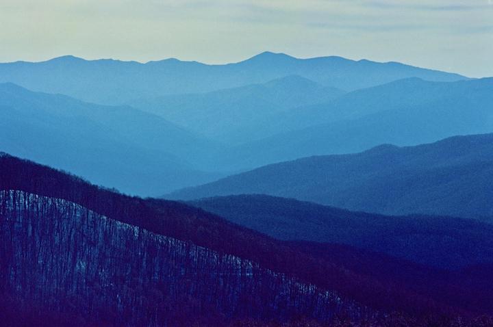 A mountain range is visible with multiple layers of blue hills and a forest in the foreground.