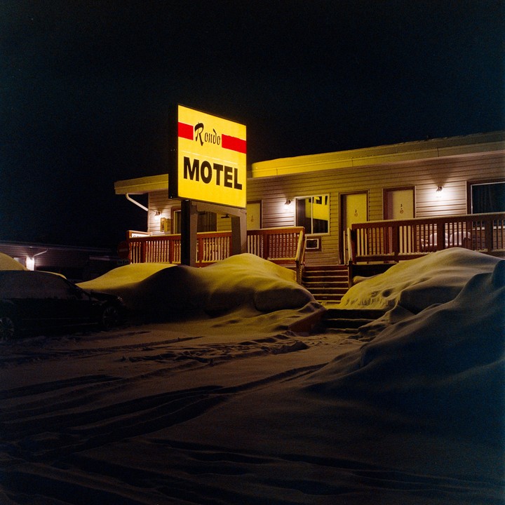 A bright yellow motel sign illuminates a snow-covered motel at night.
