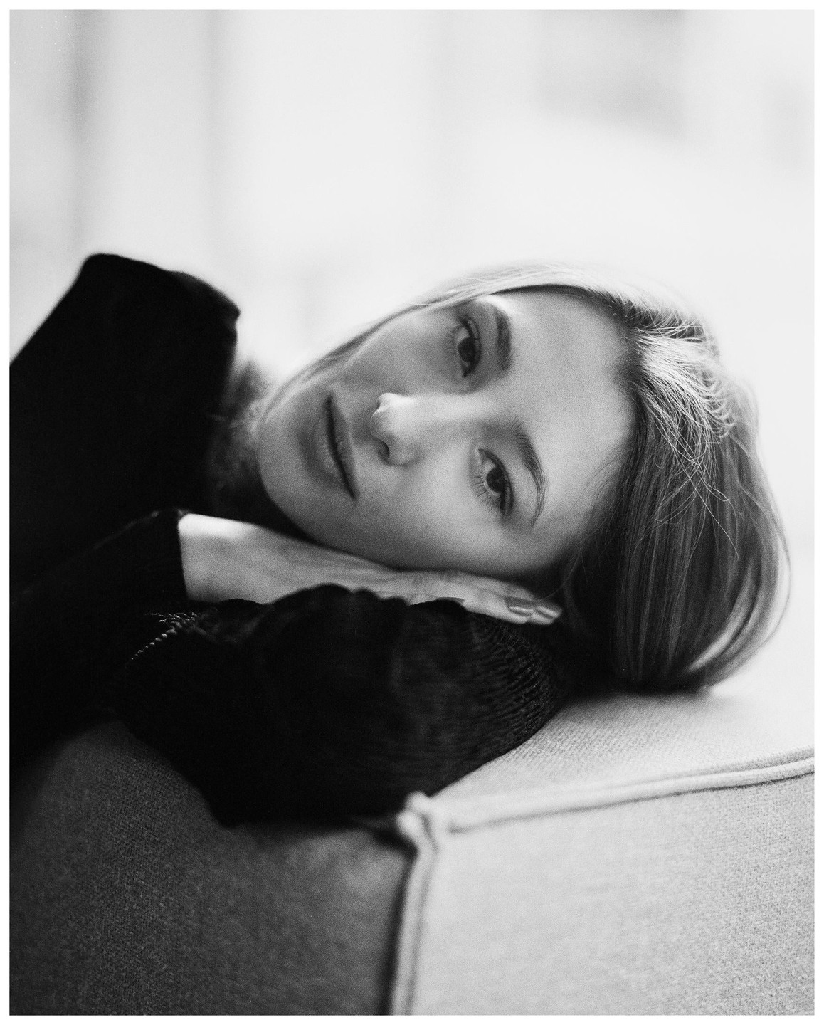 A woman with long hair rests her head on her arm on a sofa.