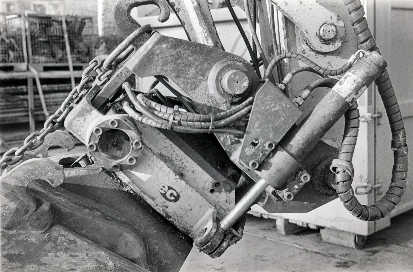 A close-up view of the hydraulic arm and bucket of an excavator shows chains, hoses, and metal components.