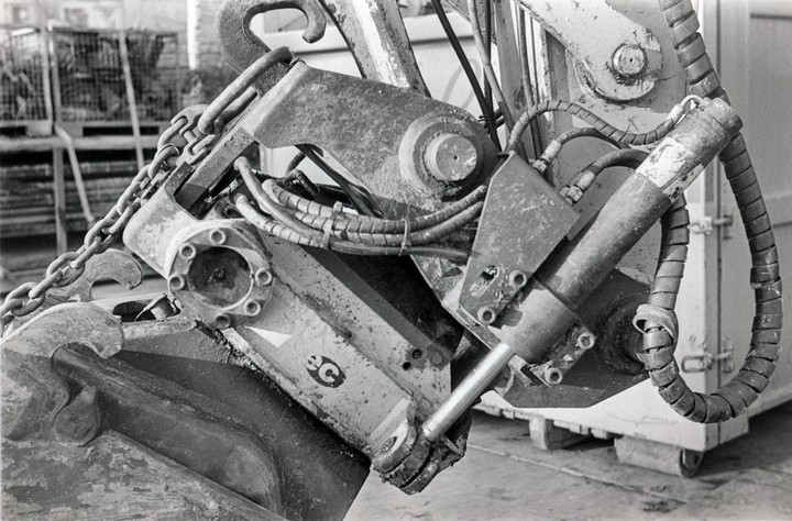 A close-up view of the hydraulic arm and bucket of an excavator shows chains, hoses, and metal components.