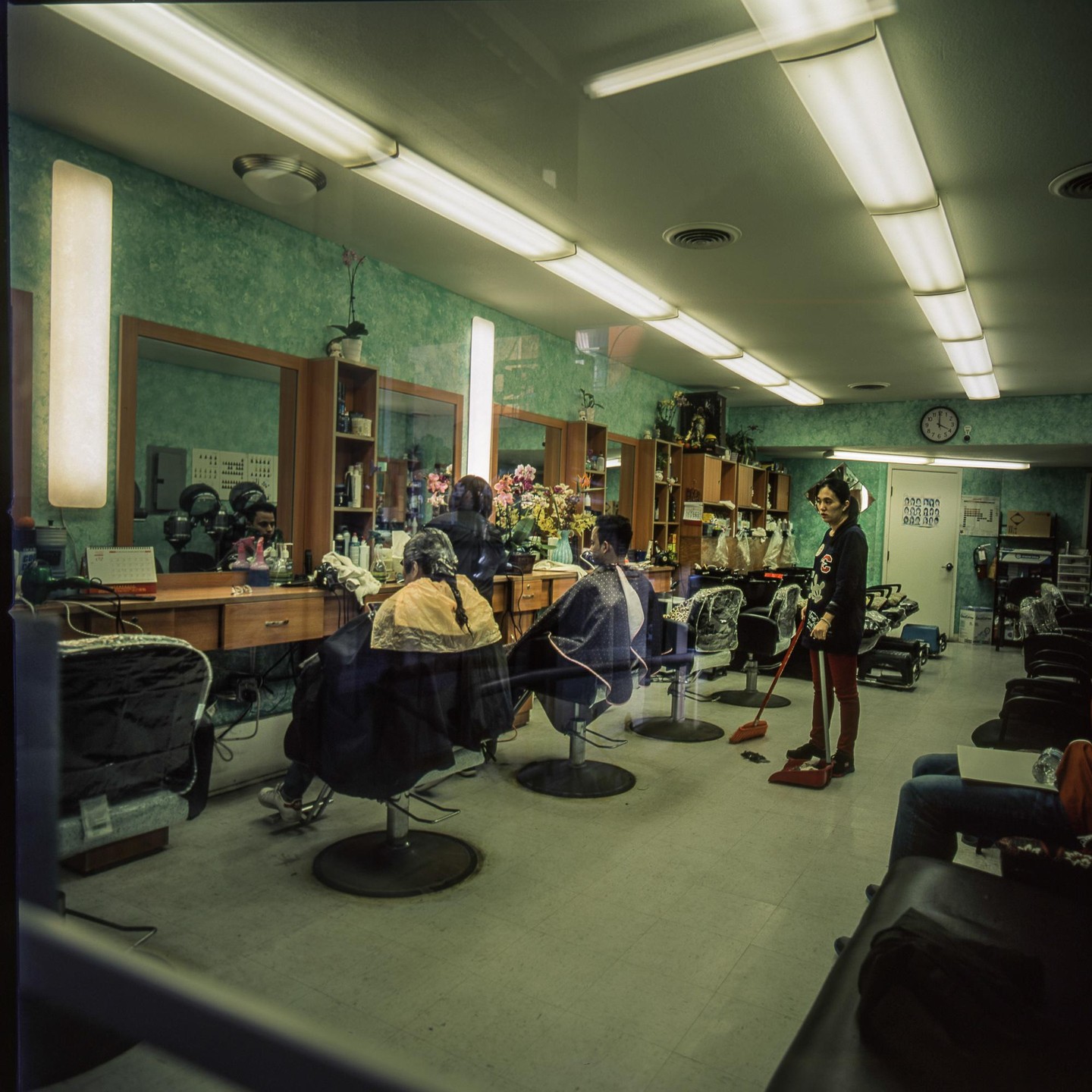A woman sweeps the floor of a barbershop where several men are getting haircuts.