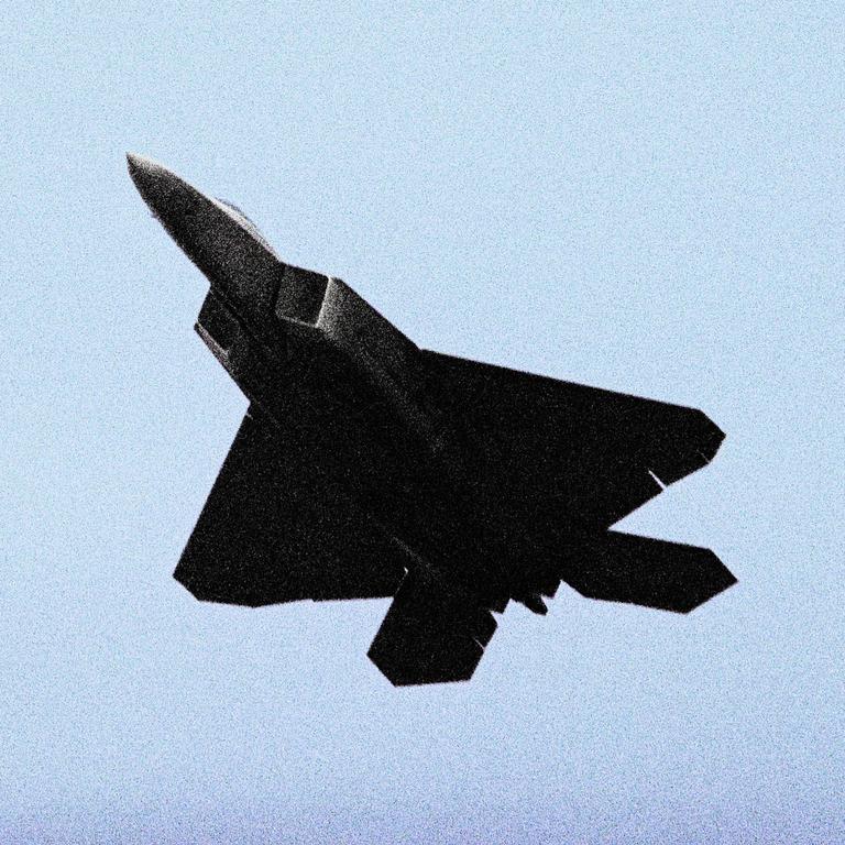 A dark fighter jet is captured against a light blue sky.