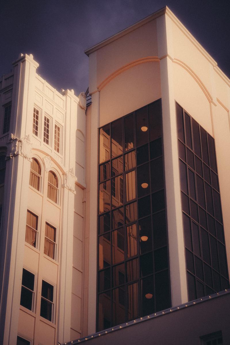 Two buildings with different architectural styles stand side by side, one with many windows and the other with a large glass facade reflecting the surroundings.
