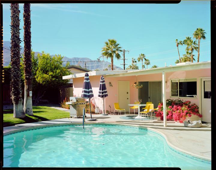 A pink house with a swimming pool and palm trees is visible under a clear sky.