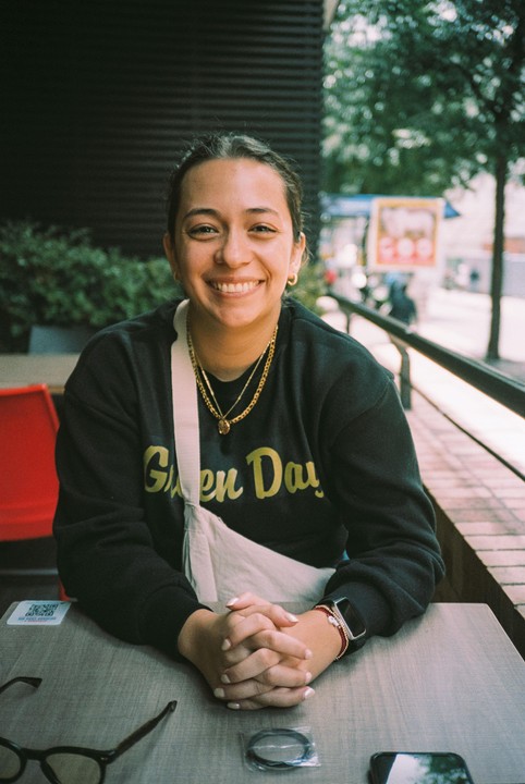 A woman with a wide smile sits at a table with her hands clasped.