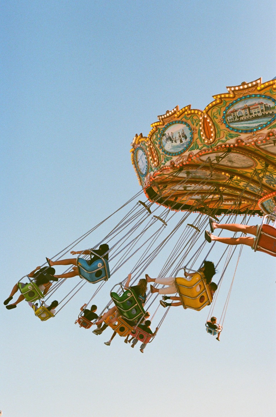 People ride a colorful swing carousel against a clear blue sky.