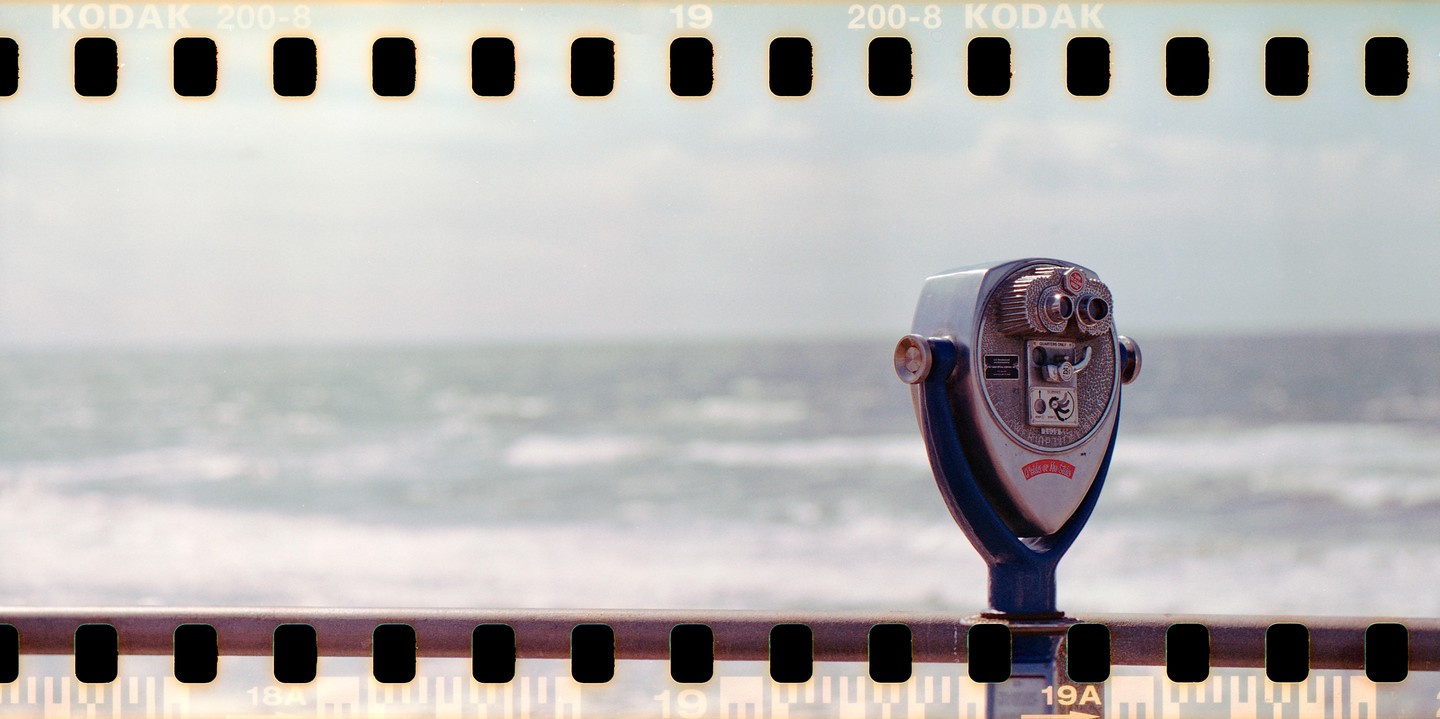 A coin-operated binocular viewer stands on a railing overlooking the ocean.