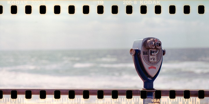 A coin-operated binocular viewer stands on a railing overlooking the ocean.