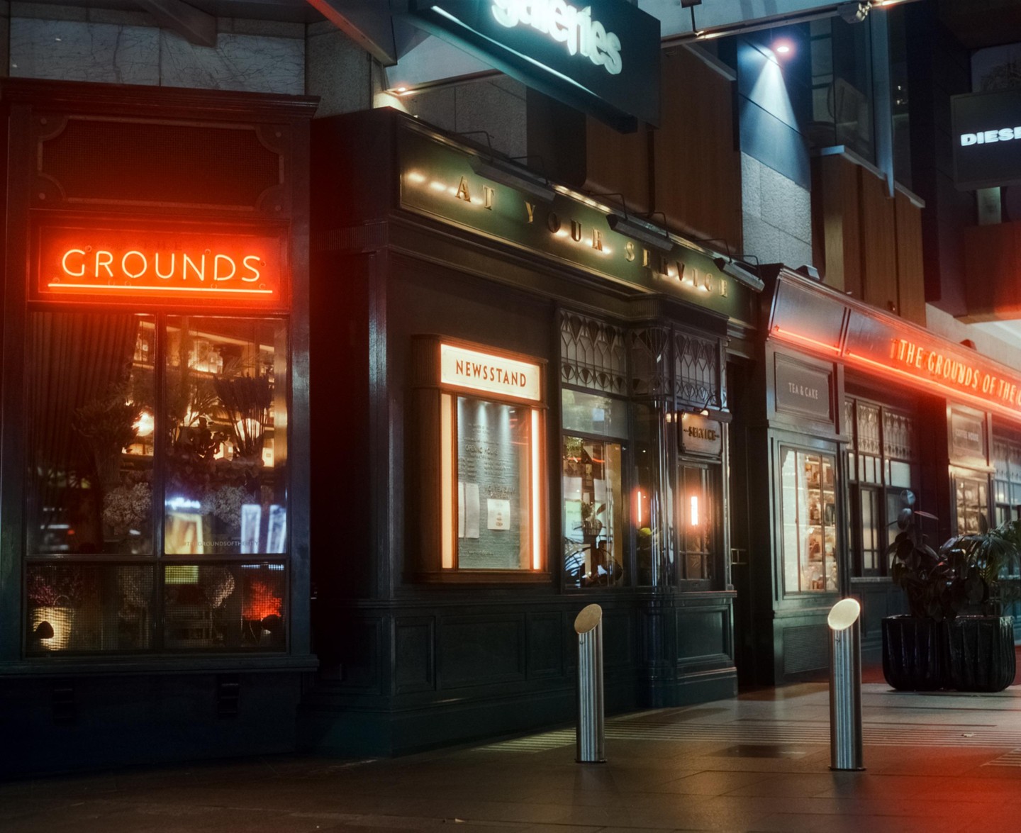 A storefront with neon signs for "Grounds" and "Newsstand" is illuminated at night.