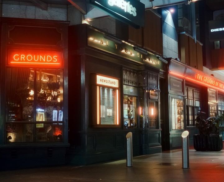 A storefront with neon signs for "Grounds" and "Newsstand" is illuminated at night.