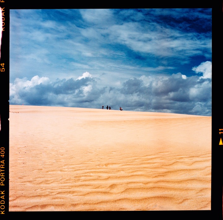 A group of people stand on a sand dune under a cloudy sky.