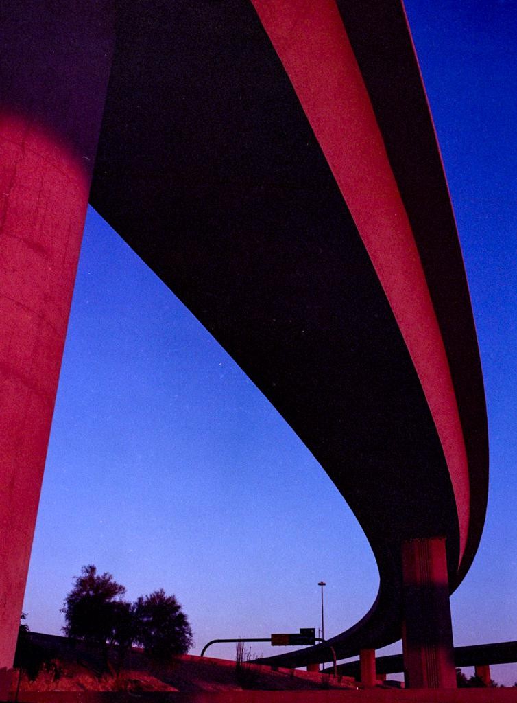 A highway overpass curves against a blue night sky, illuminated by red light from below.