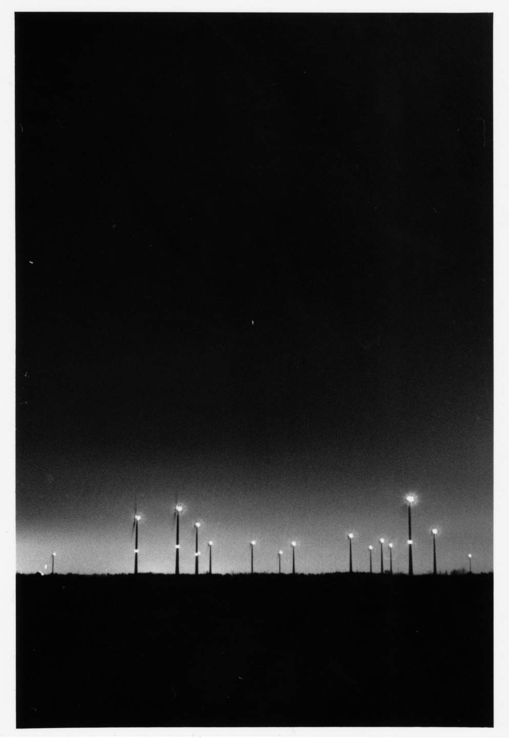 A field of wind turbines is silhouetted against a dark sky at dusk.