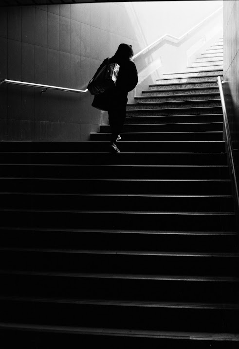 A person with a backpack walks up a dark staircase towards a bright light.