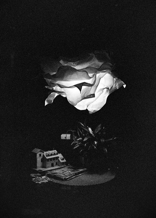 A paper lantern illuminates a miniature house, a plant, and a book on a table in a dark room.