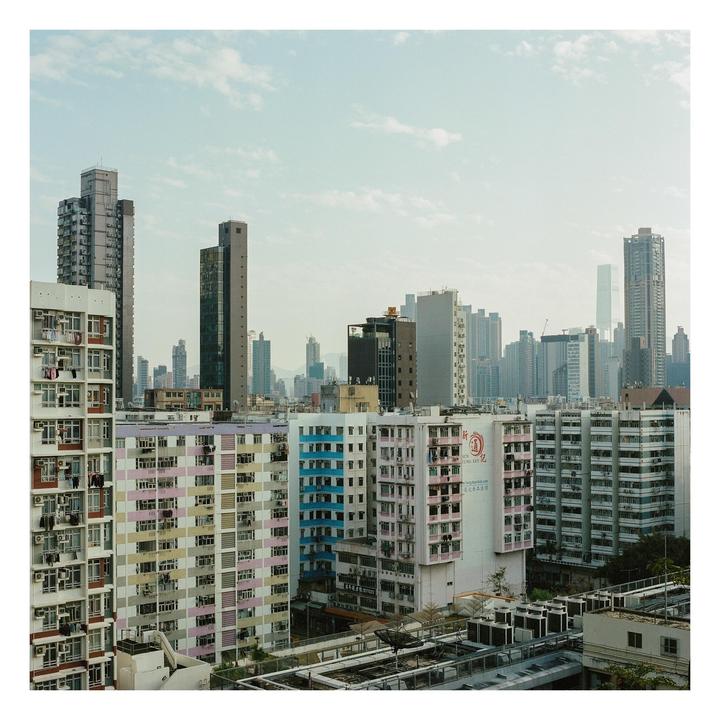 A dense urban landscape features numerous residential and commercial buildings under a cloudy sky.
