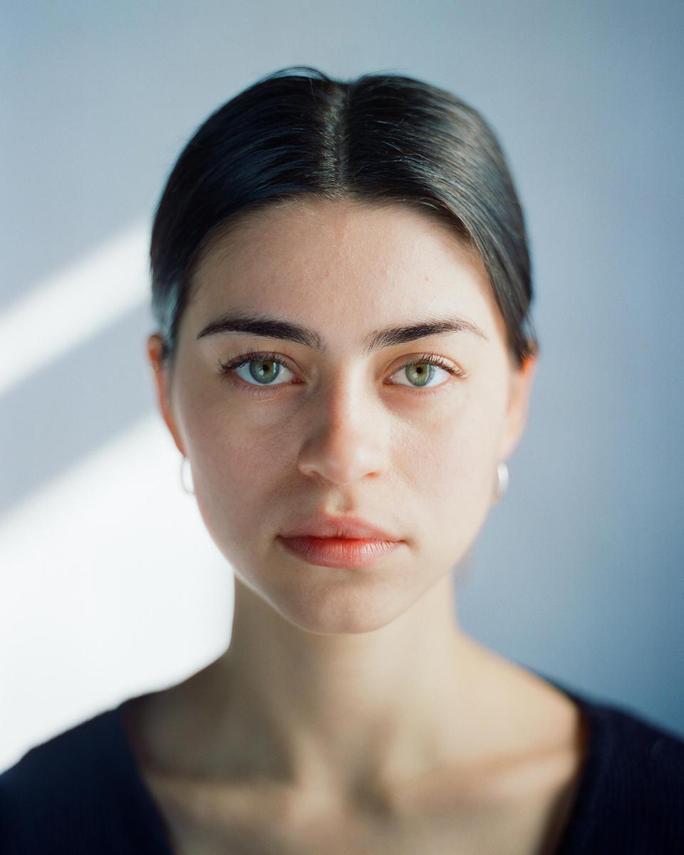 A woman with dark hair and light eyes looks directly at the viewer.