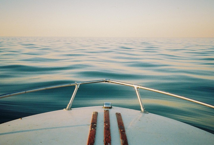 The bow of a boat is visible on a calm body of water under a clear sky.