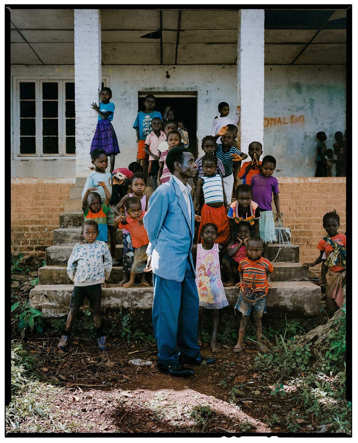 A man in a blue suit stands among a large group of children on the steps of a building.