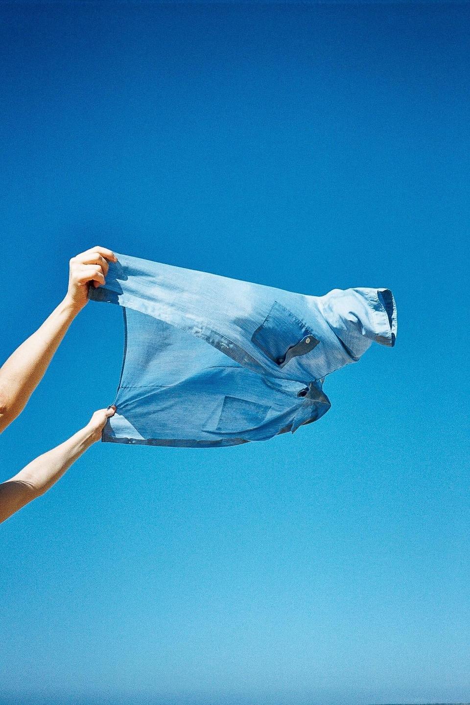 Two arms hold a blue shirt against a clear blue sky.