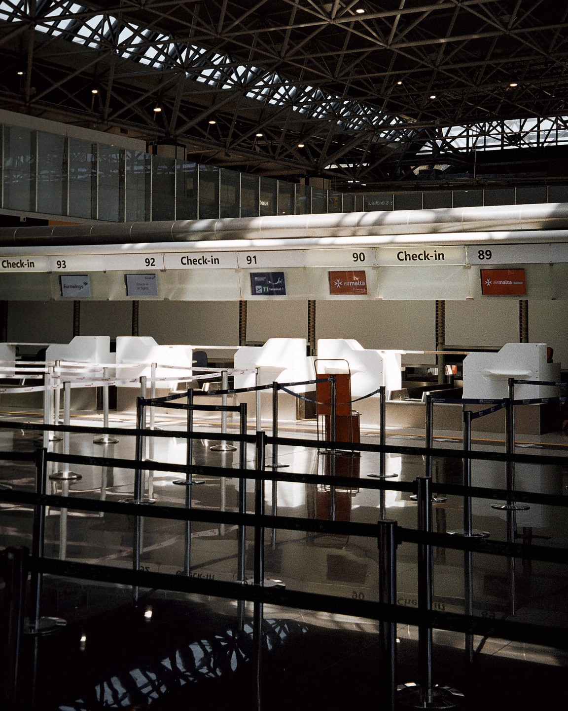 An empty airport check-in area is visible with numbered counters and a metal ceiling structure.