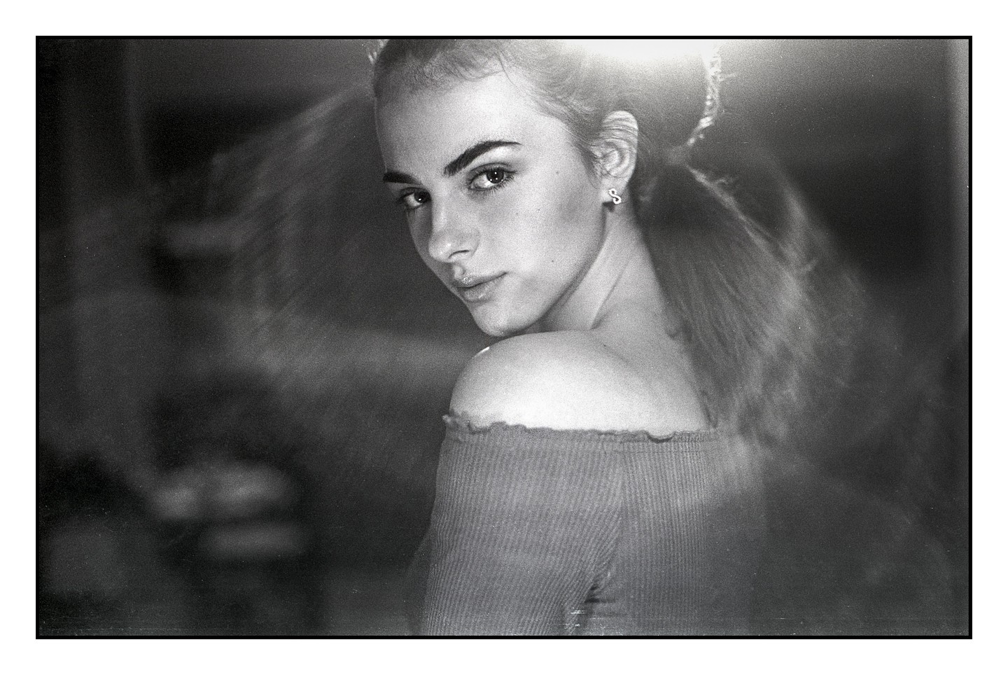 A woman with her hair tied back looks over her shoulder at the viewer.