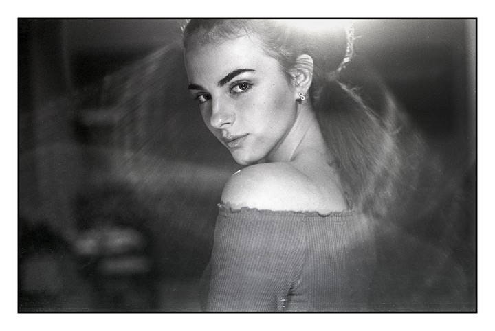 A woman with her hair tied back looks over her shoulder at the viewer.