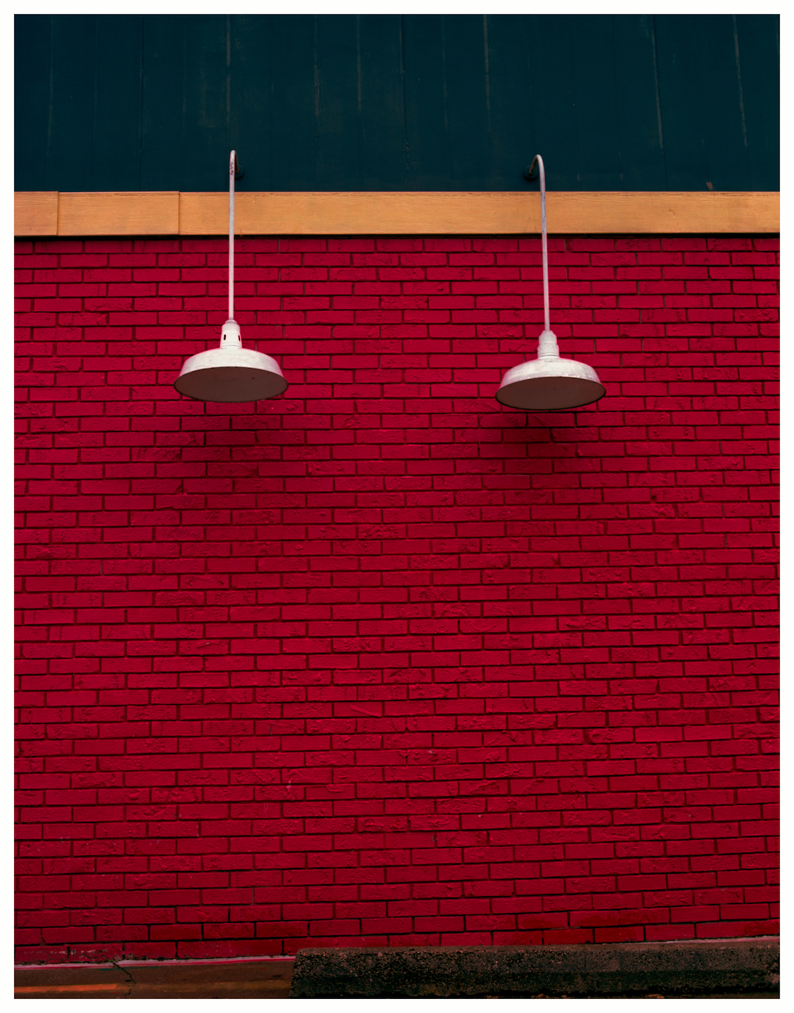 Two white lamps hang against a vibrant red brick wall, topped by a dark blue wooden facade.