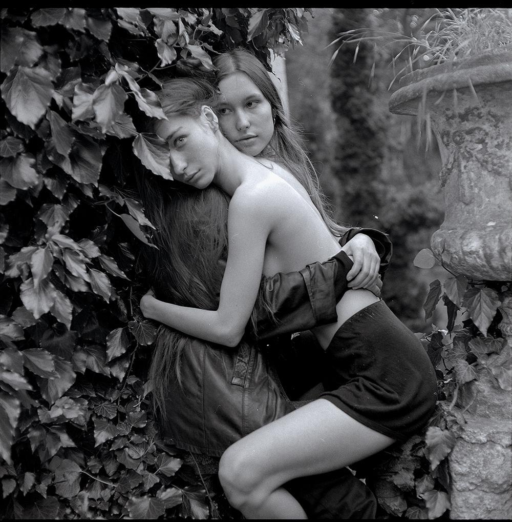 Two women are embracing each other while surrounded by ivy and a stone planter.