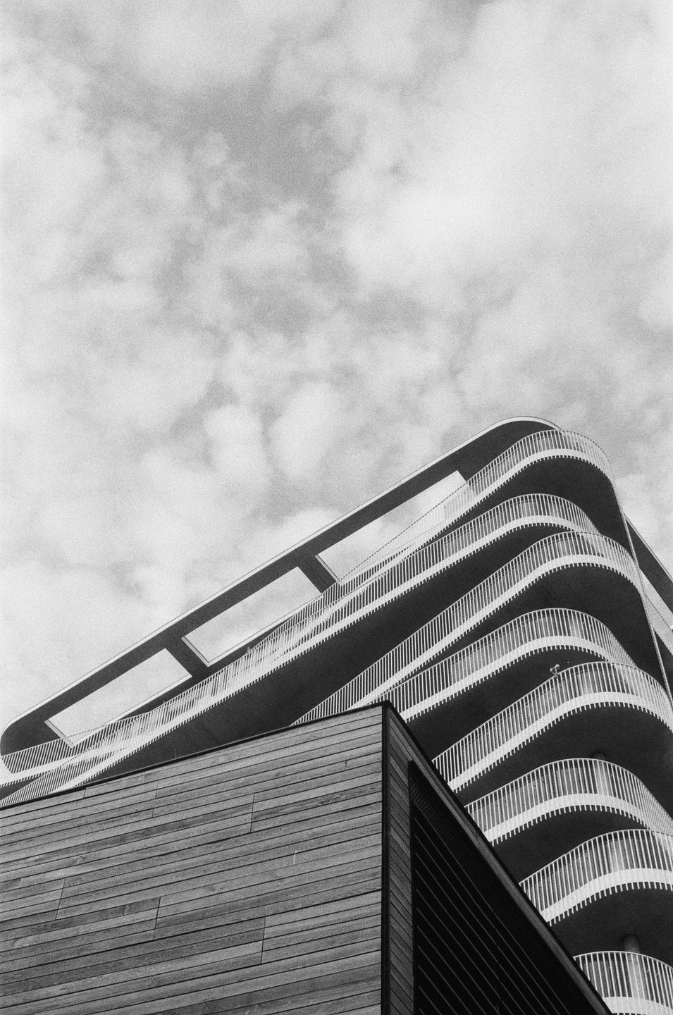 A low-angle view shows a modern building with curved balconies and a section clad in wood.