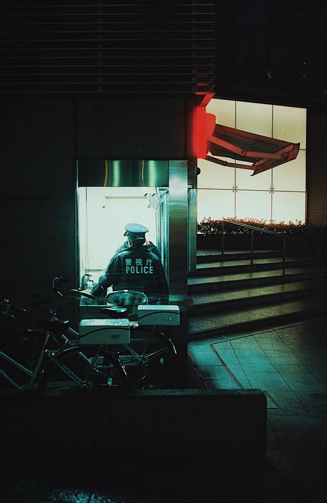 A police officer sits in a brightly lit booth next to a bicycle at night.