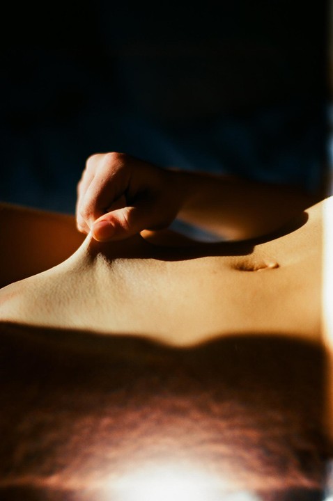 A hand pinches the skin of a stomach, with a belly button visible.