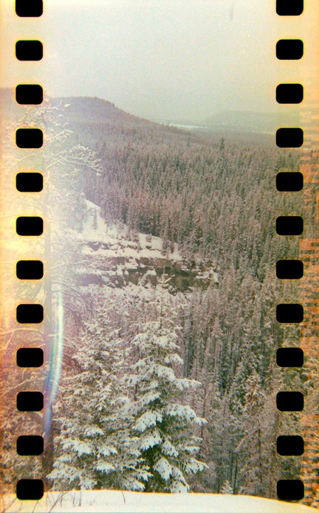 A snow-covered forest stretches across a valley with a rocky cliff face visible in the middle ground.