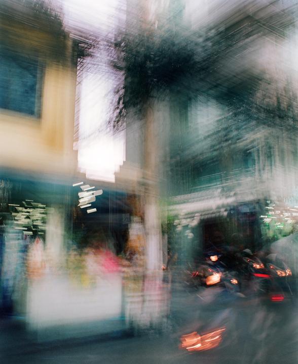 A blurry street scene shows buildings, a tree, and a motorcycle with glowing lights.