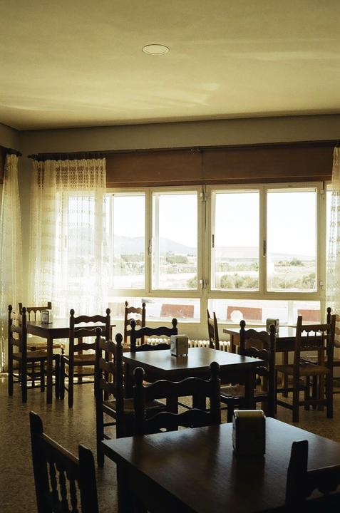 A brightly lit room with several empty wooden tables and chairs is visible through a large window.