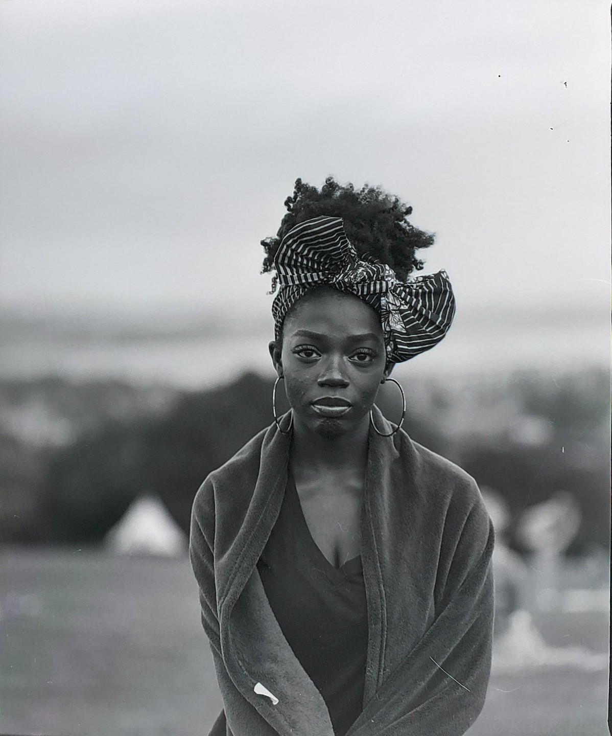 A woman wearing a head wrap and large hoop earrings looks directly at the viewer.