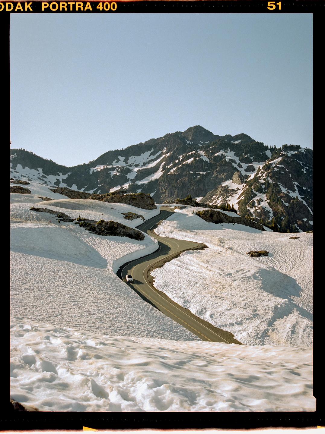 A winding road cuts through a snow-covered mountain landscape under a clear sky.