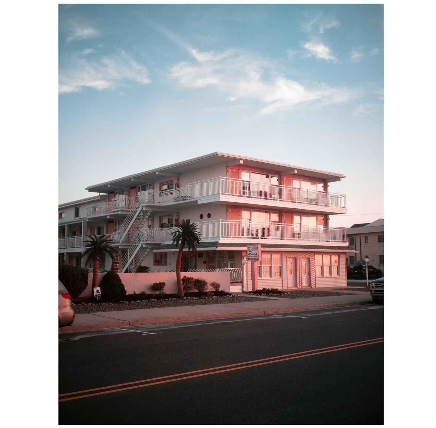 A three-story motel with balconies and palm trees is illuminated by the golden hour light.