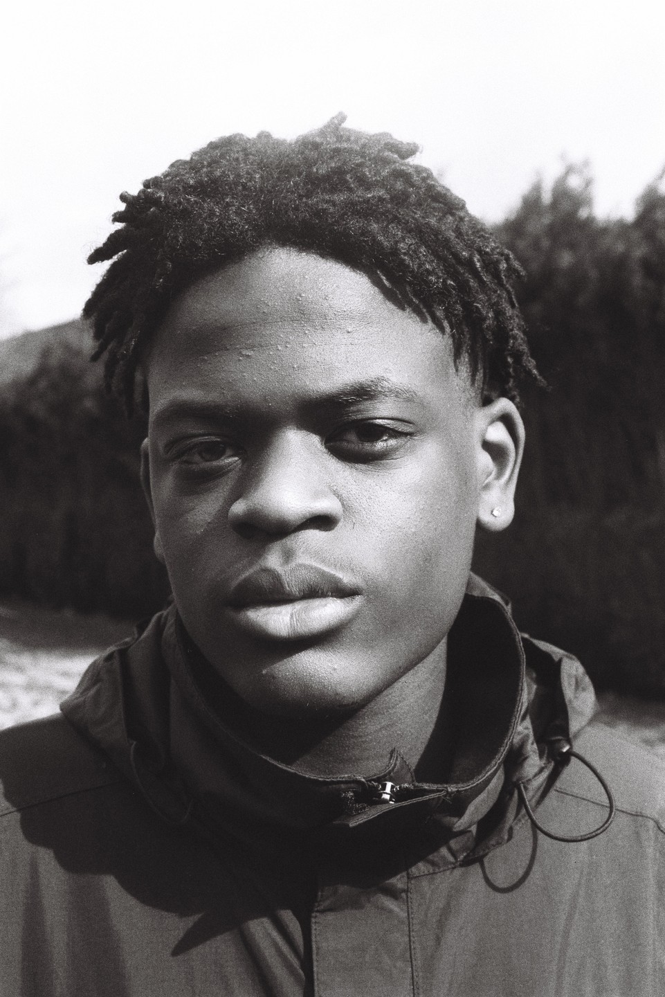 A young man with dreadlocks looks directly at the viewer.