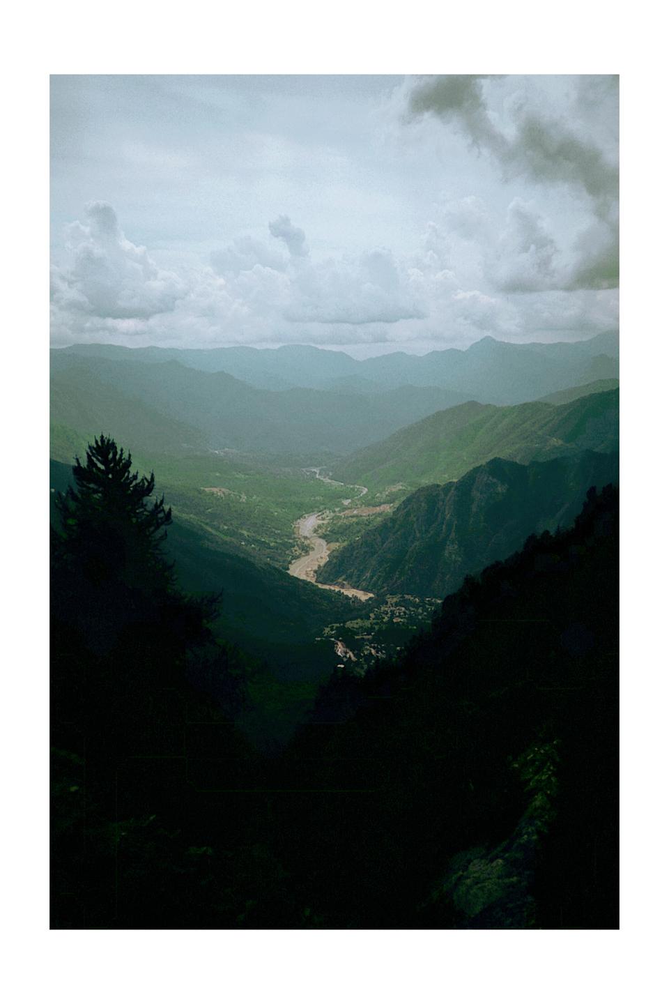 A winding river flows through a deep valley surrounded by mountains under a cloudy sky.
