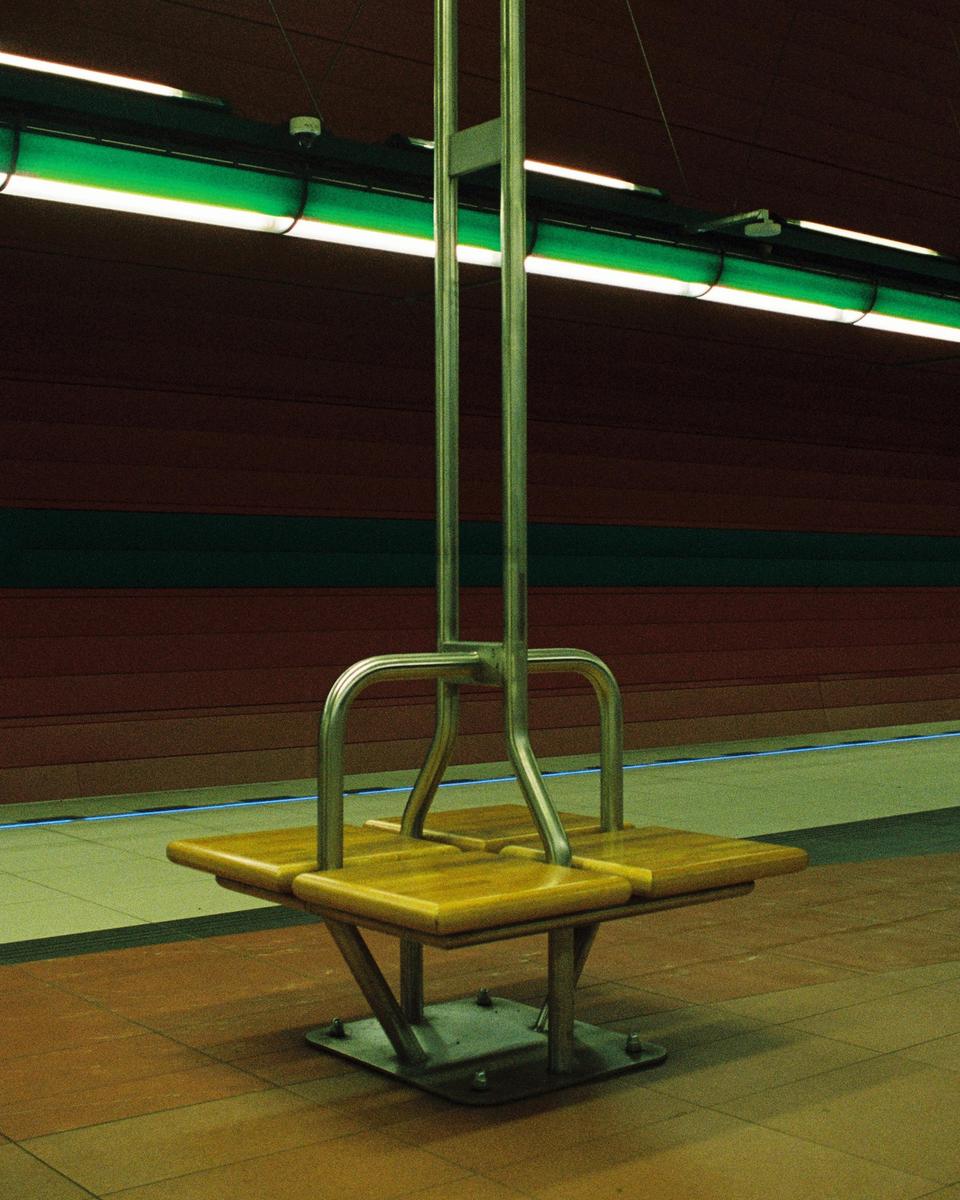 A wooden and metal bench sits on a tiled floor in a subway station.