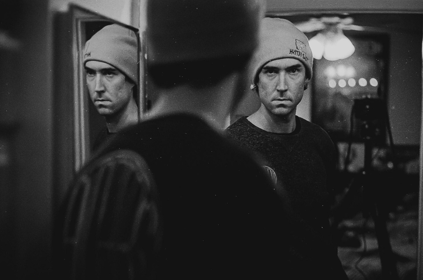 A man wearing a beanie looks at his reflection in a mirror.