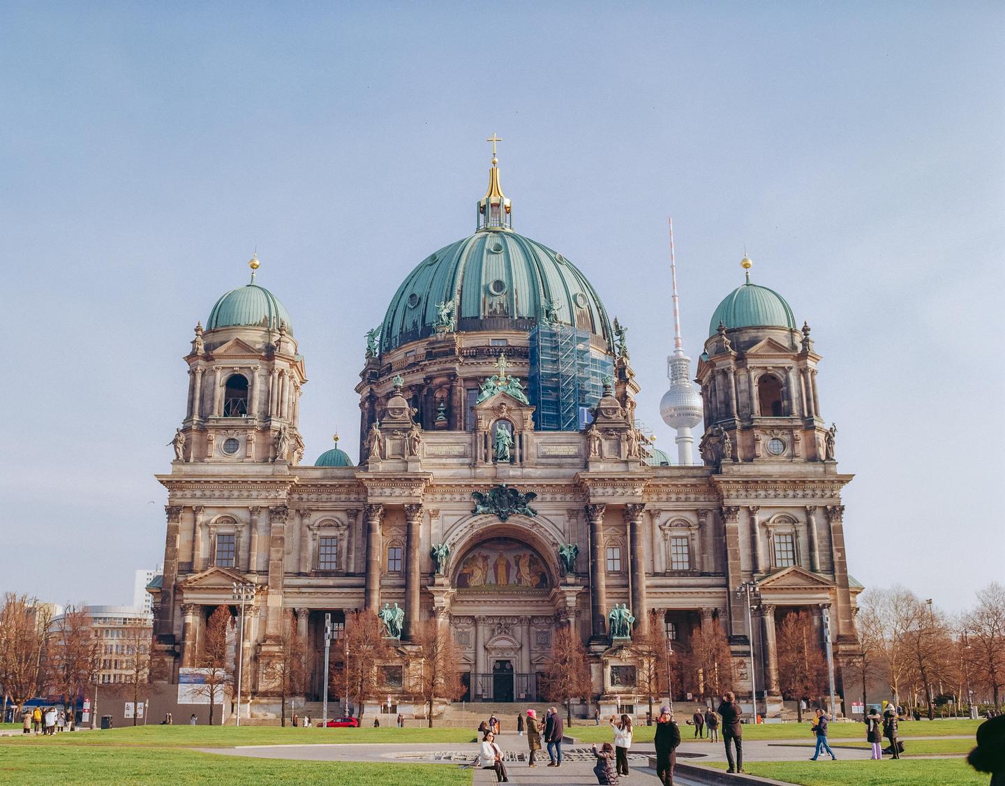 The Berliner Dom, a large cathedral with a green dome and two smaller green-domed towers, stands prominently with a television tower visible in the background.
