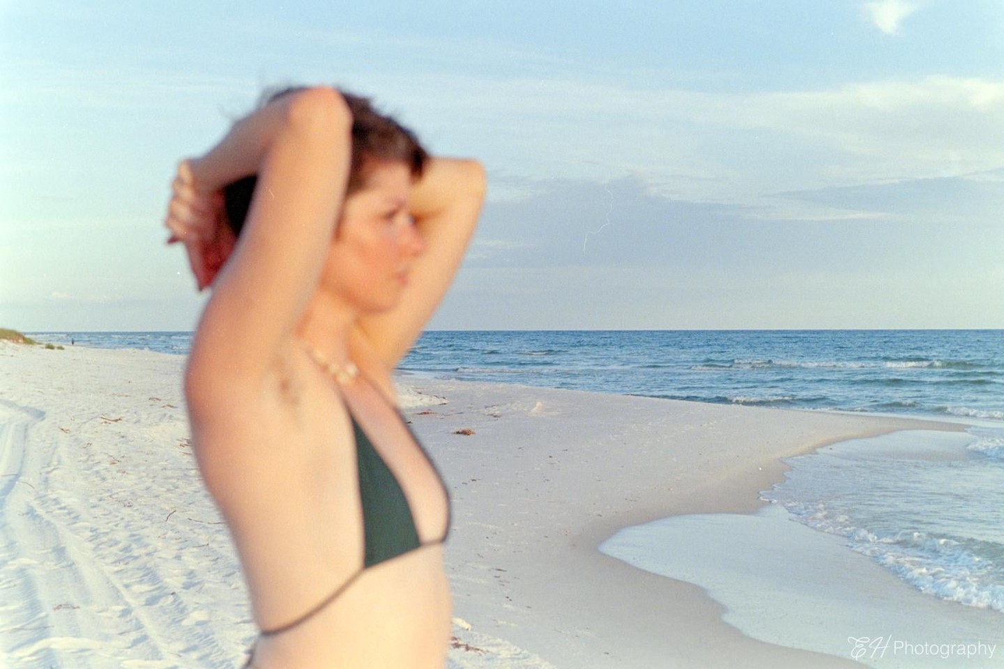 A woman in a bikini stands on a white sand beach with the ocean in the background.