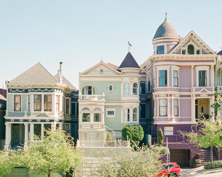 A row of colorful Victorian houses with intricate architectural details stands under a clear sky.