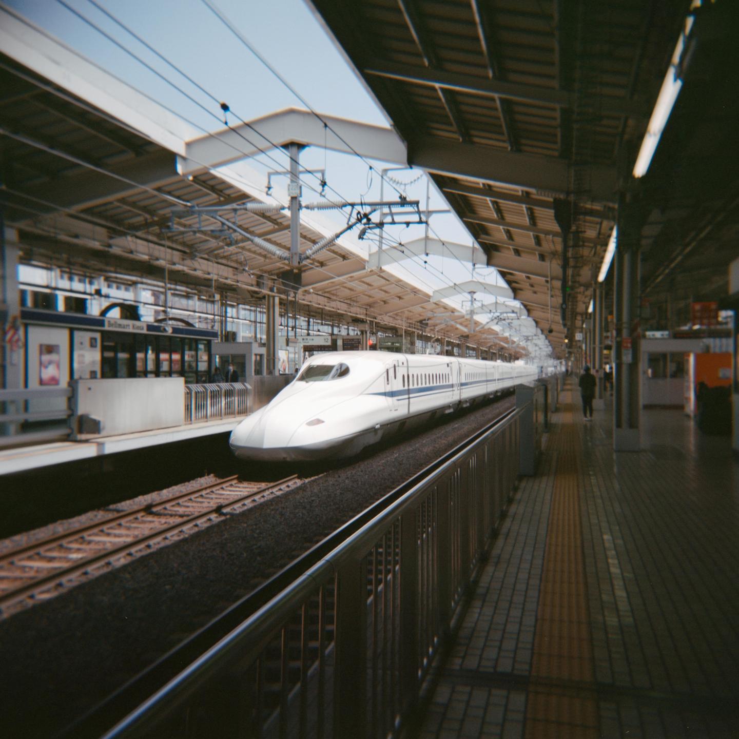 A white bullet train is stopped at a station platform with a person walking in the distance.