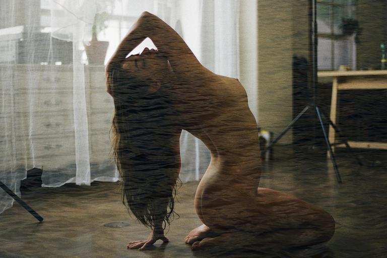 A woman with long hair is kneeling on the floor with her back arched and arms raised above her head, created with a double exposure effect that makes her body appear to be made of water.